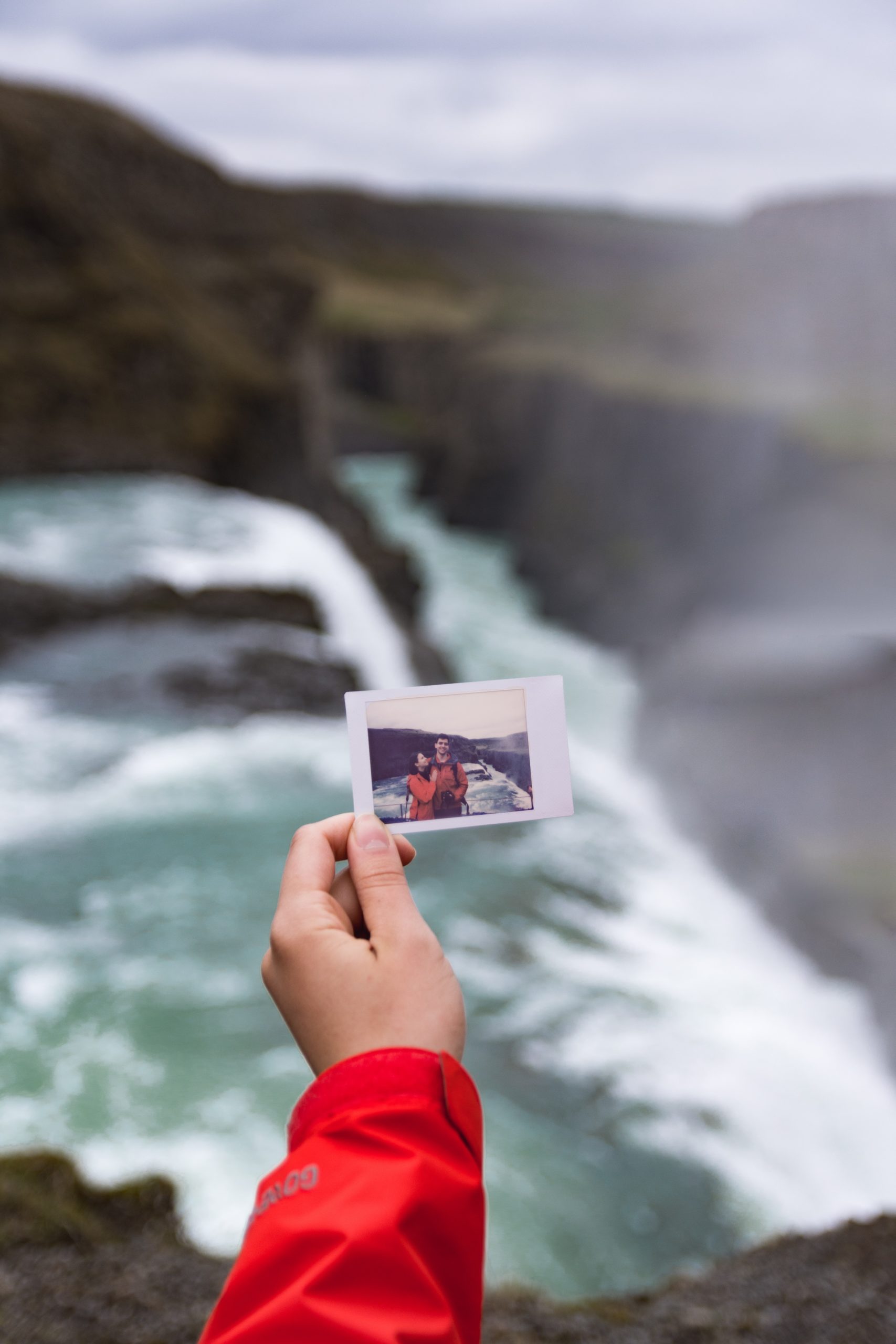 A polaroid picture of a couple in front of Gullfoss Waterfall, with Gullfoss Waterfall in the background